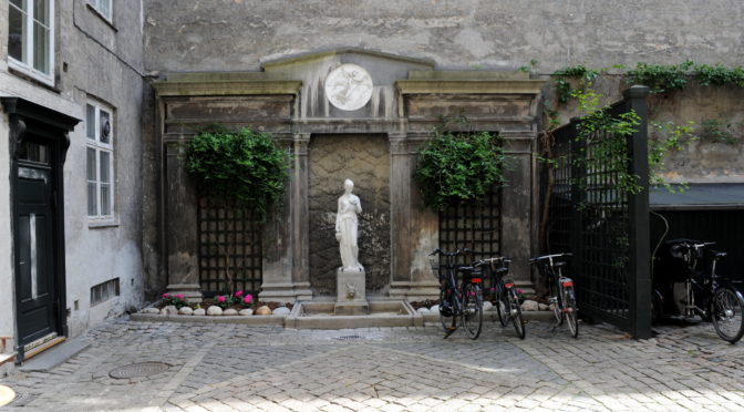 Skulptur af marmor foran facade formet som forsiden af et antik tempel - i en baggråd med cykler